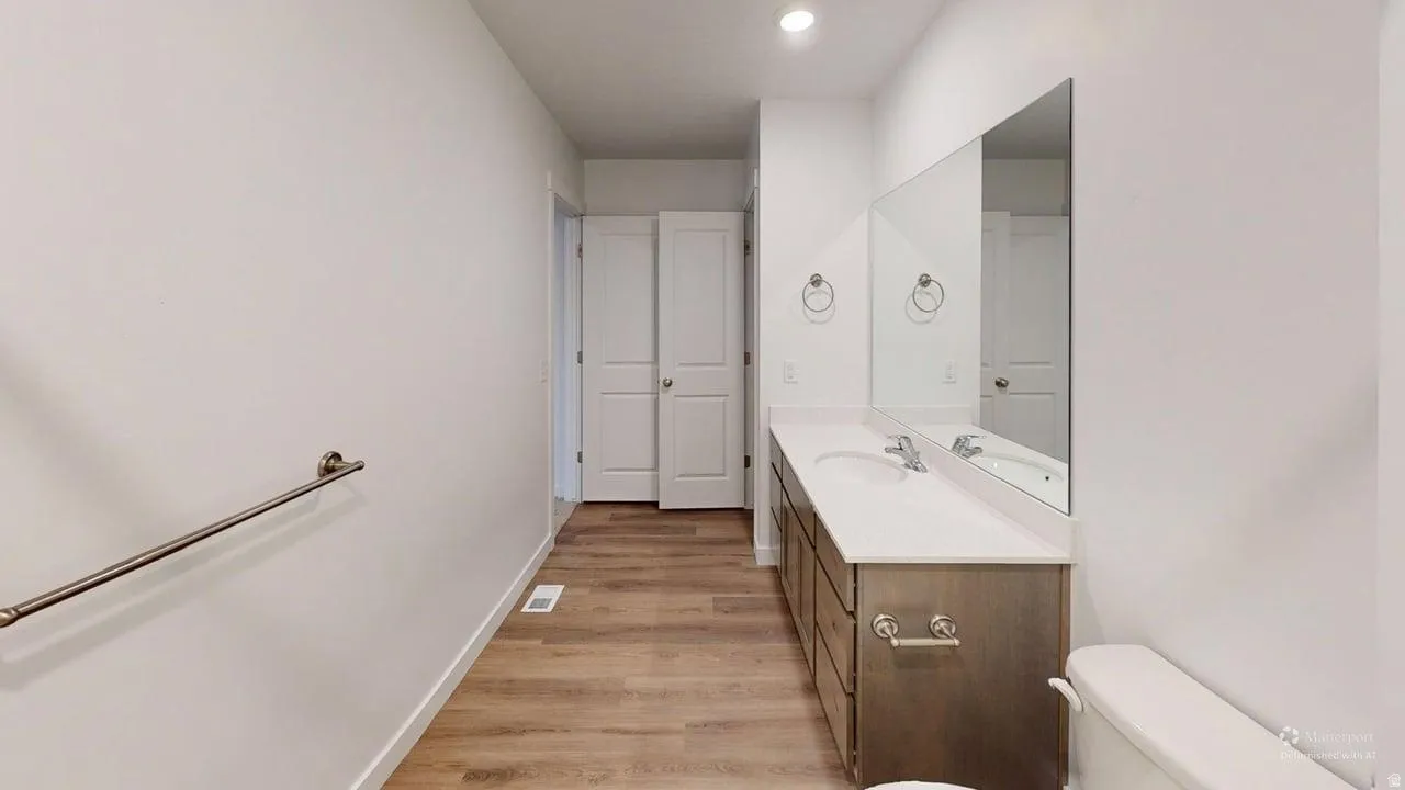 Bathroom featuring a double vanity with undermount sinks, a large mirror, a toilet, and wood-finish flooring