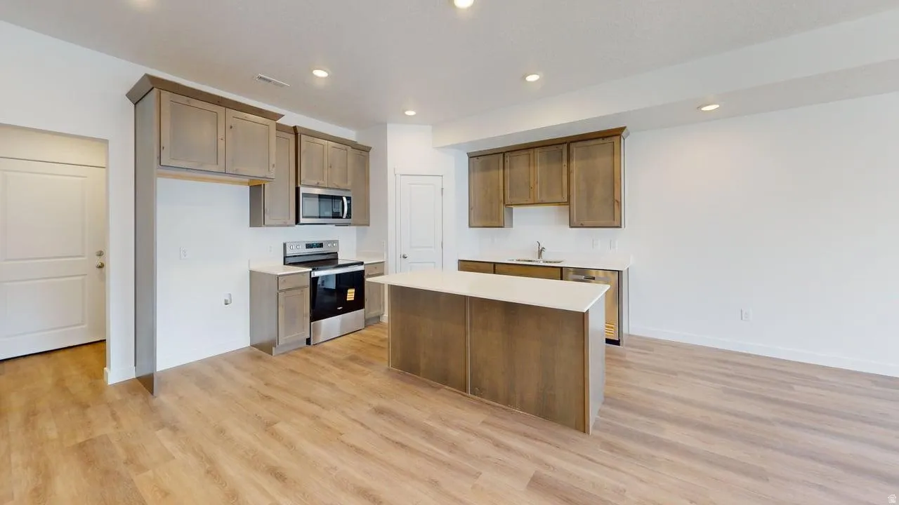 Kitchen featuring wood-finish flooring, shaker-style cabinetry, stainless steel appliances, a center island with a white countertop, and recessed lighting