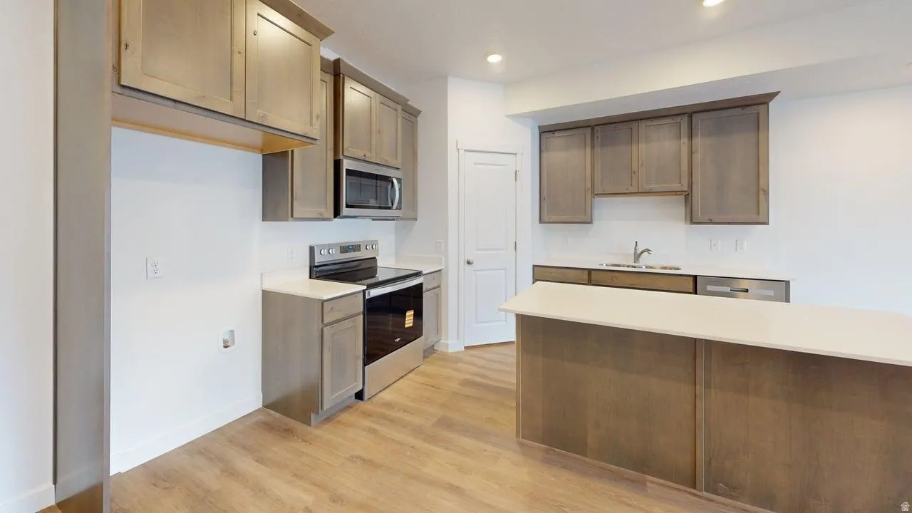 Contemporary kitchen featuring wood-finish flooring, light wood-tone cabinetry, stainless steel appliances, a white subway tile backsplash, and an island with a light-toned countertop