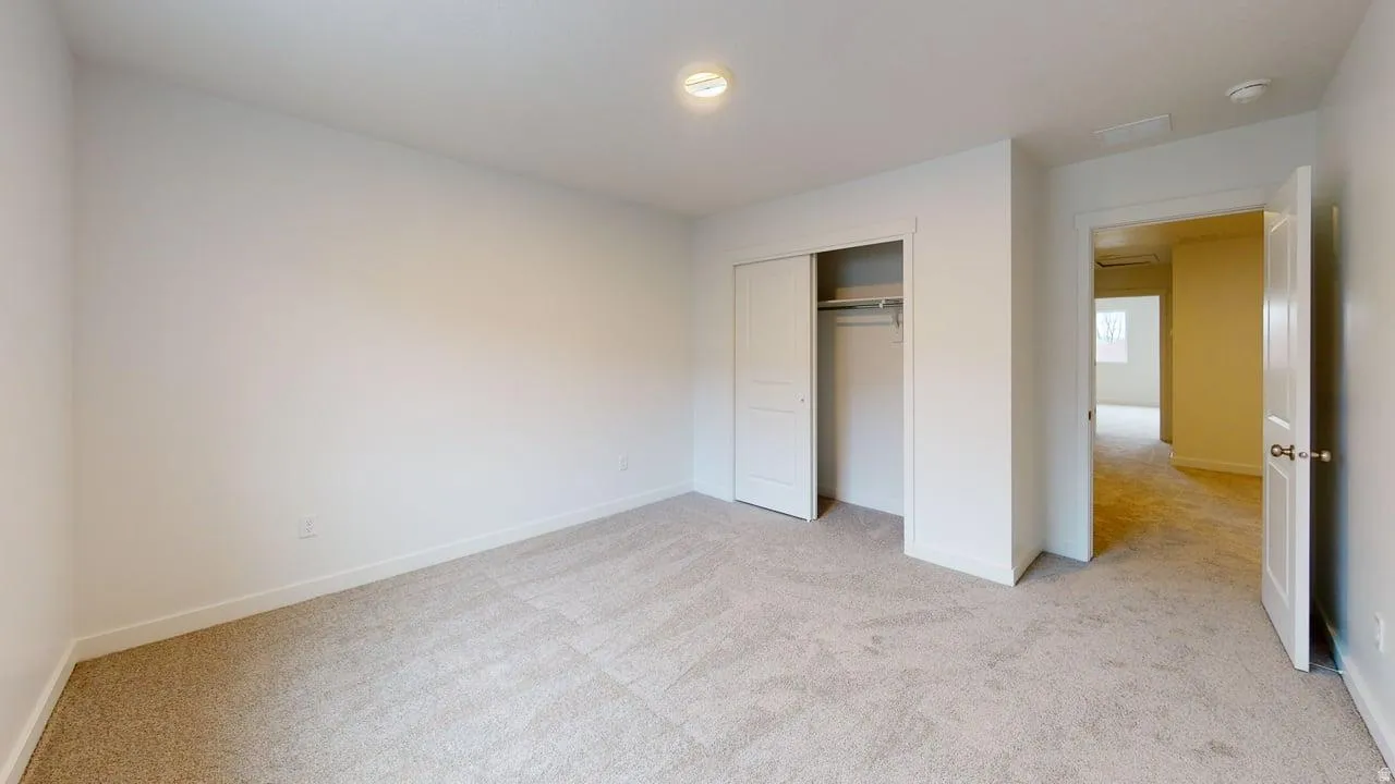 Carpeted room featuring white walls, a flush-mount ceiling light, and a bi-fold closet with an interior rod