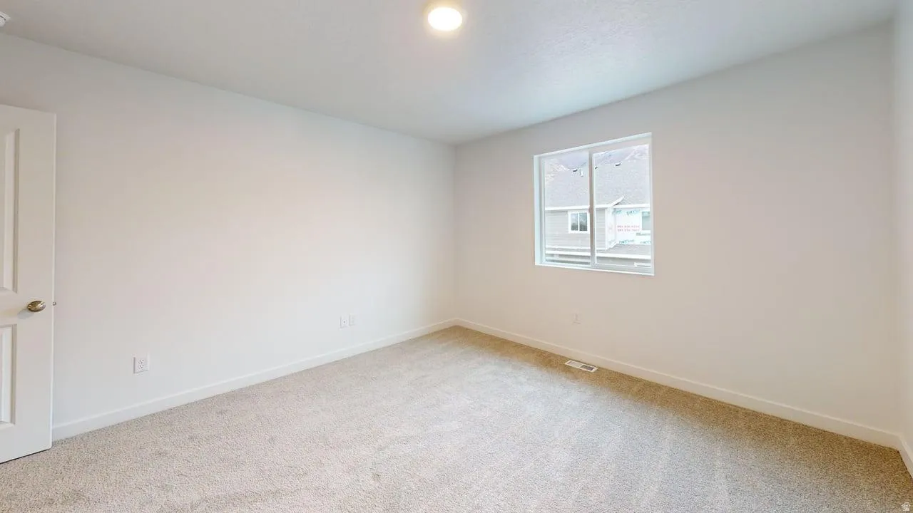 Neutral-toned carpeted room featuring a single window, white walls, and a white interior door with a brass-toned knob