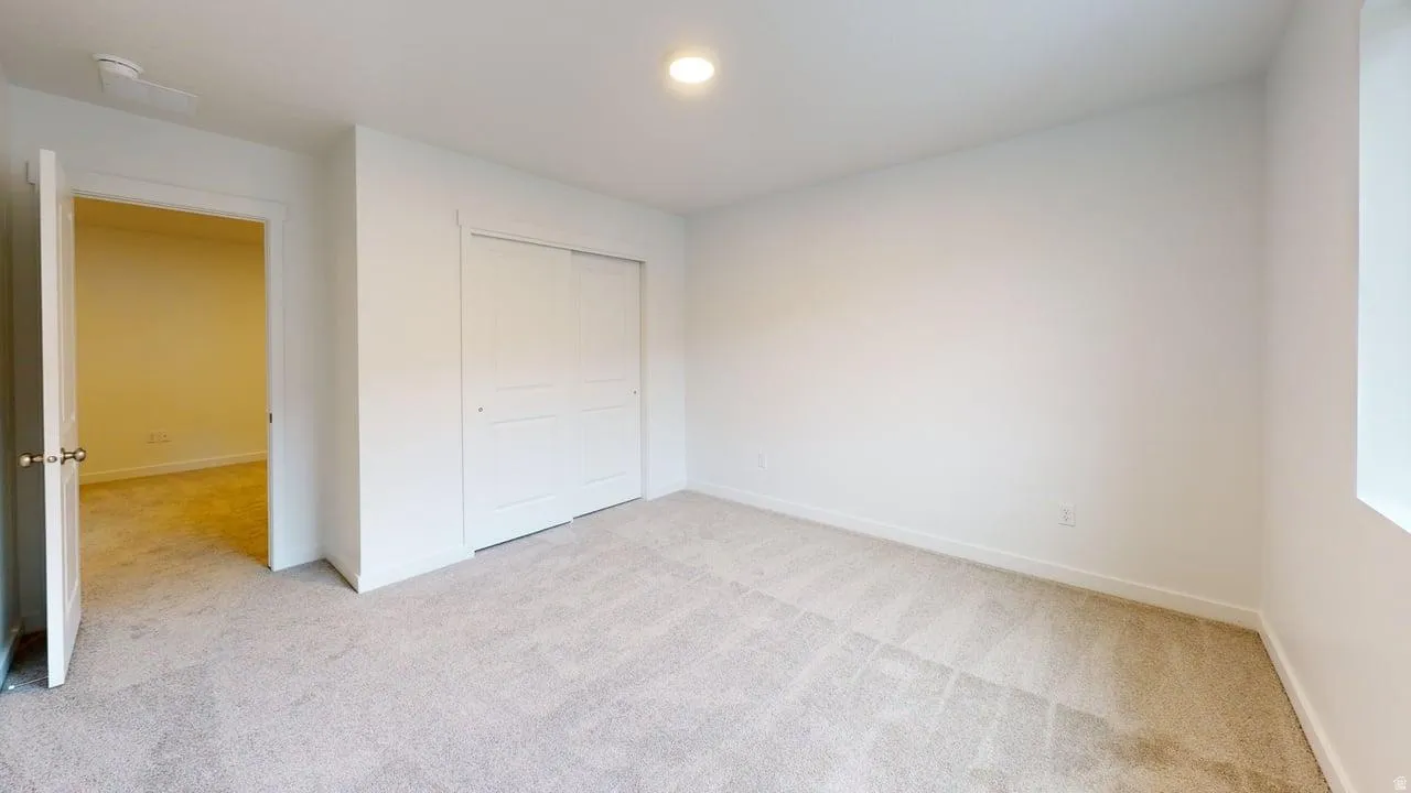 Carpeted interior space featuring white walls, a single window, an open doorway, and a closet with sliding panel doors