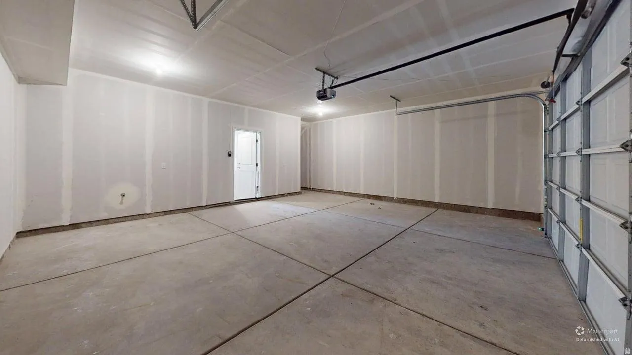 Spacious garage with exposed concrete flooring, unfinished drywall, and a white interior door