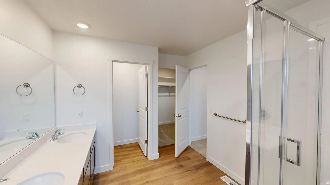 Bathroom featuring a double vanity with integrated sinks, a glass-enclosed shower, wood-finish flooring, and recessed lighting