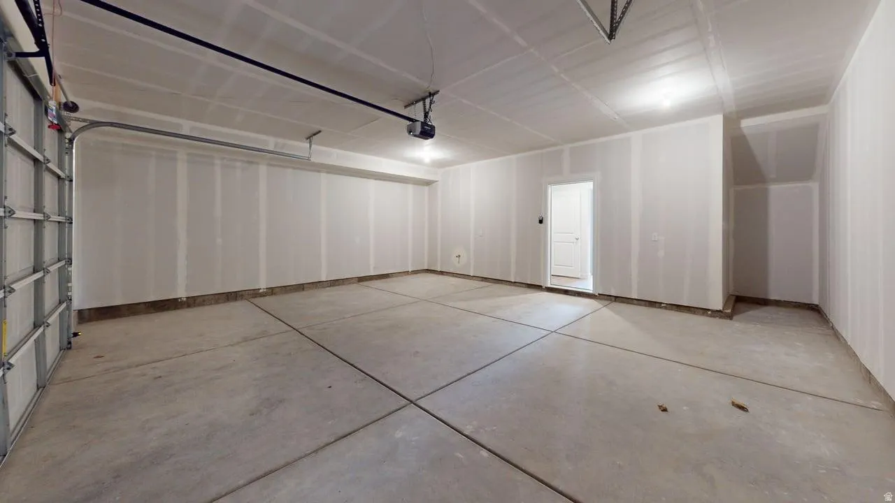 Spacious garage featuring a concrete floor, high ceilings, exposed drywall, and a white interior door