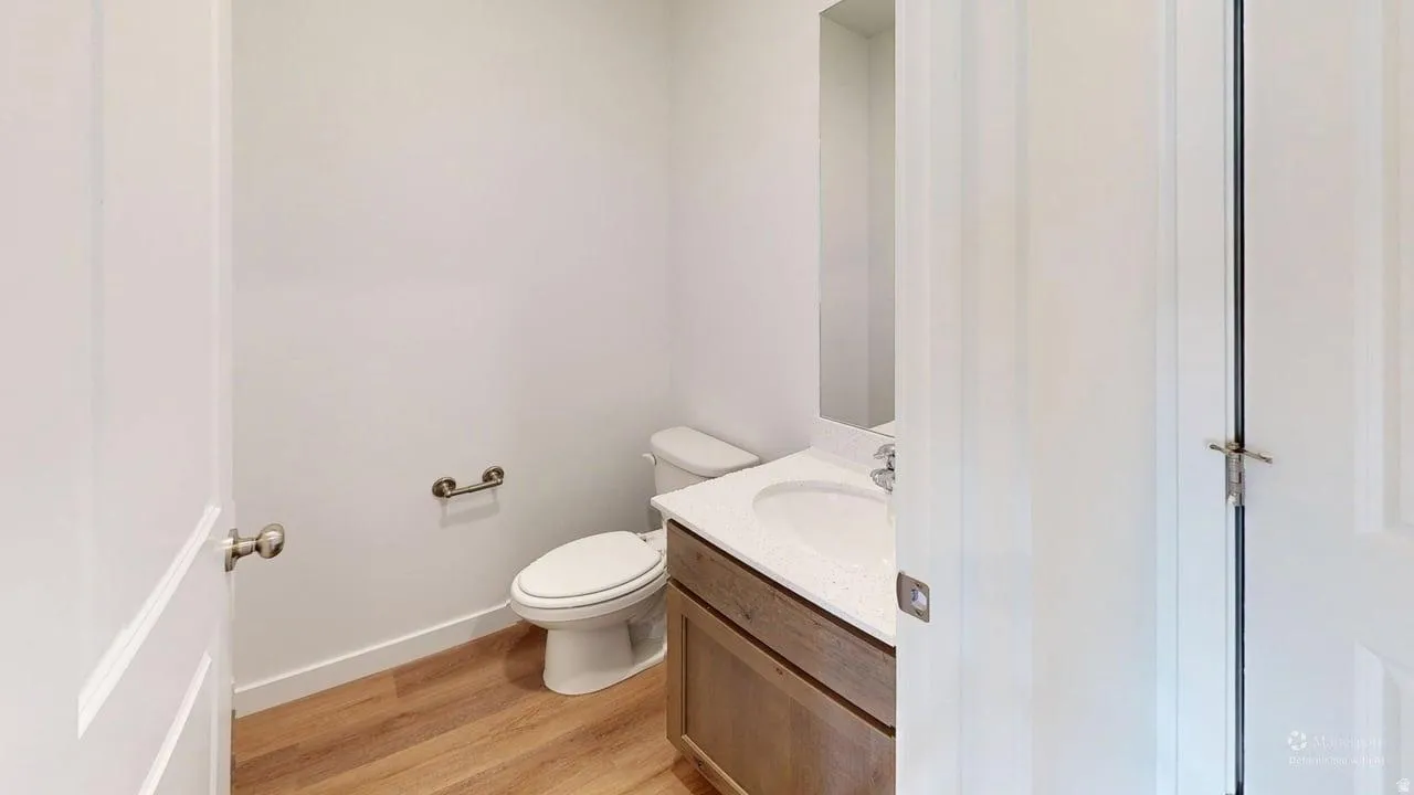 Powder room featuring a single vanity with an integrated sink, wood-finish flooring, and a wall-mounted mirror