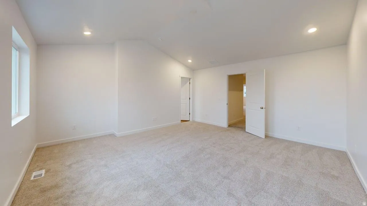 Spacious room featuring light-toned carpeting, white walls, recessed lighting, and a window providing natural light