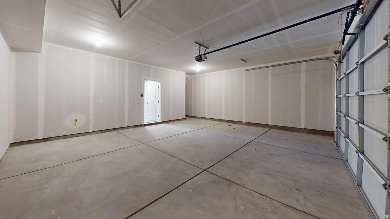 Spacious garage featuring a concrete floor, exposed drywall walls, recessed ceiling lighting, an automatic overhead door, and an interior access door