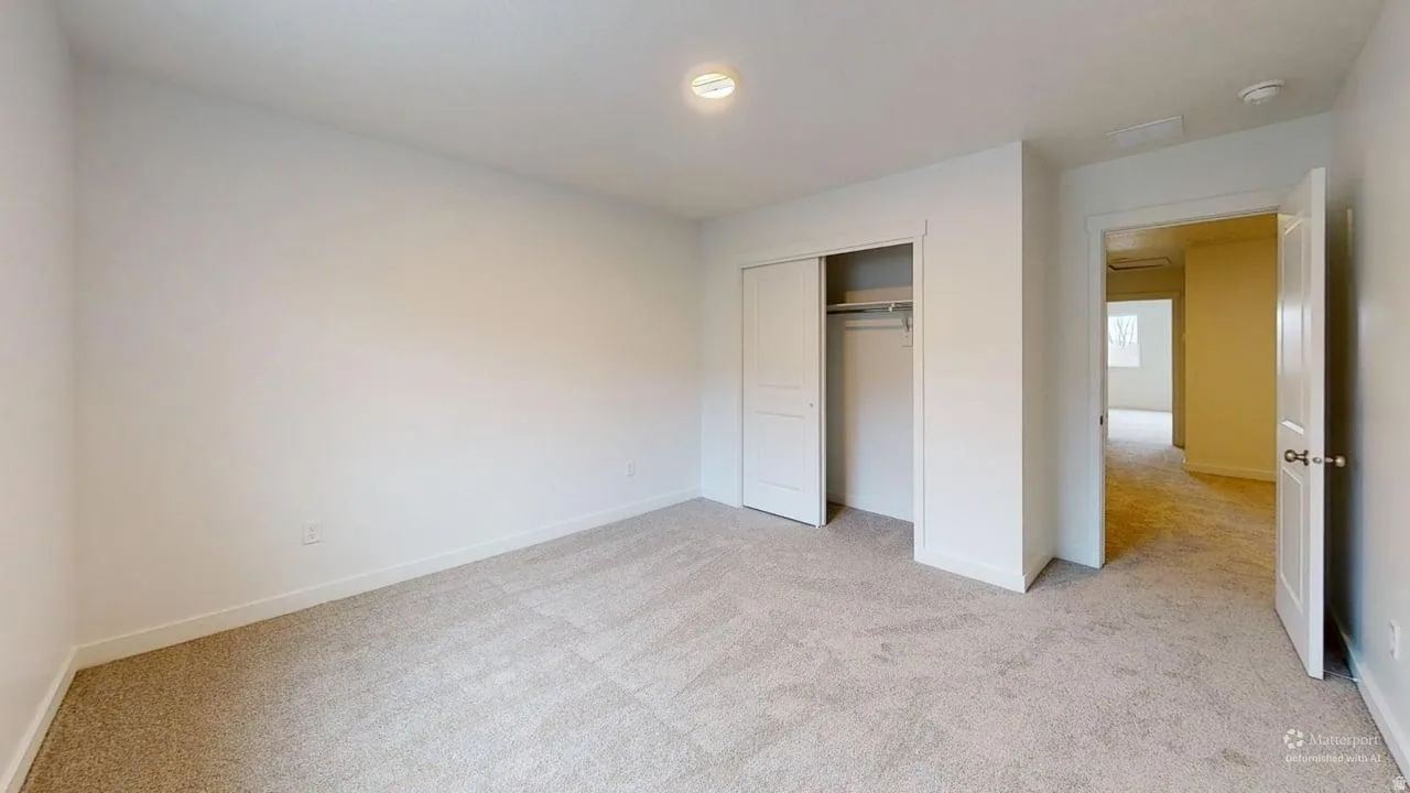 Carpeted room with white walls, featuring a bi-fold closet with hanging rod, a flush-mount ceiling light, and white trim throughout