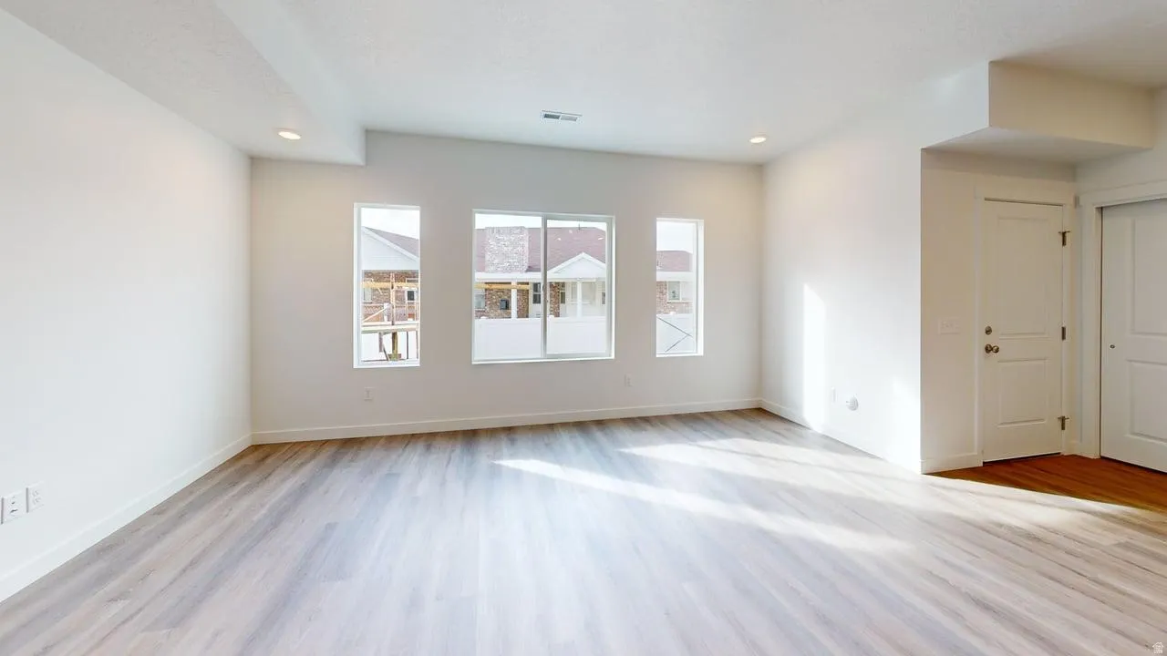 Spacious interior featuring wood-finish flooring, ample natural light from multiple windows, recessed lighting, and crisp white walls