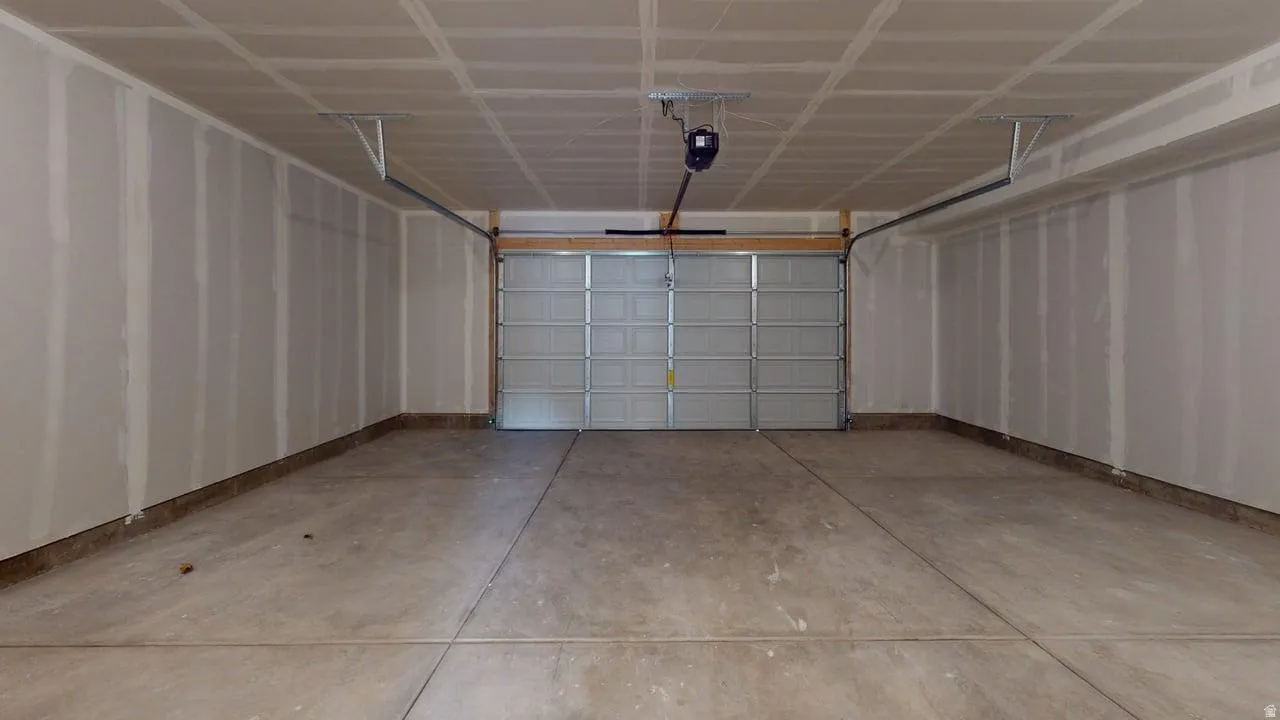 Spacious garage featuring a concrete floor, an overhead garage door opener, and unfinished drywall walls