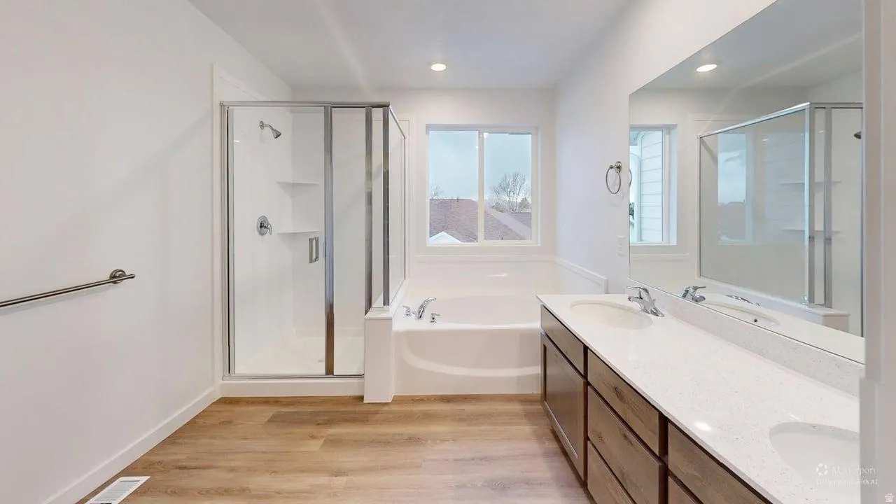 Contemporary bathroom featuring a dual vanity with light-colored countertops, a built-in tub, a separate glass-enclosed shower, and wood-finish flooring