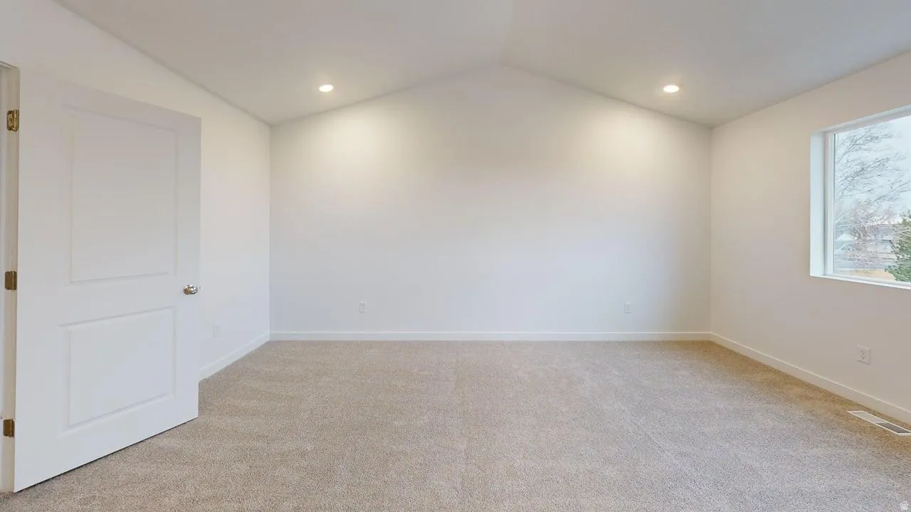 Spacious room featuring vaulted ceilings, light neutral carpeting, recessed lighting, and a single window with white trim