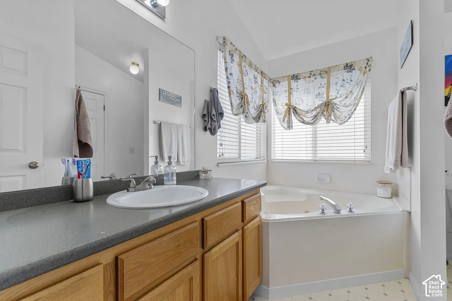 Bathroom featuring a spacious corner soaking tub with chrome fixtures, a wood-finish vanity, and a large integrated sink