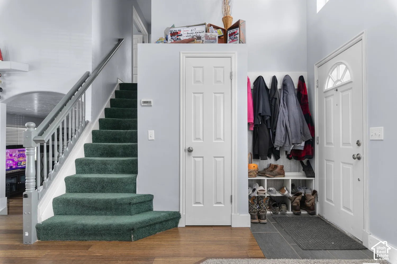 Entryway featuring wood-finish flooring, a carpeted staircase with painted wood railing, a built-in shoe and coat rack, and a front entry door with an arched window