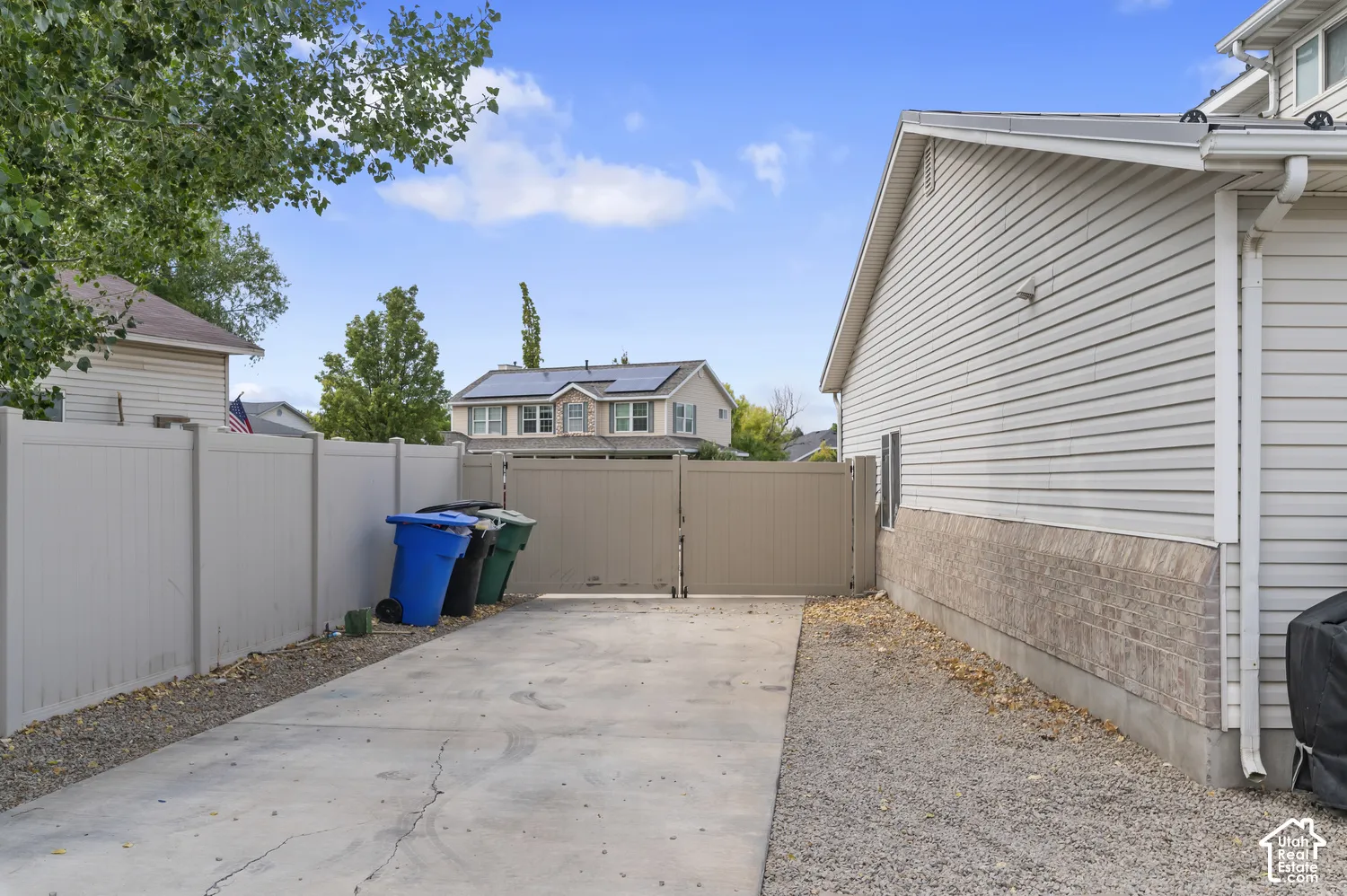 Concrete driveway with gravel border, alongside a light-colored privacy fence and matching double gates