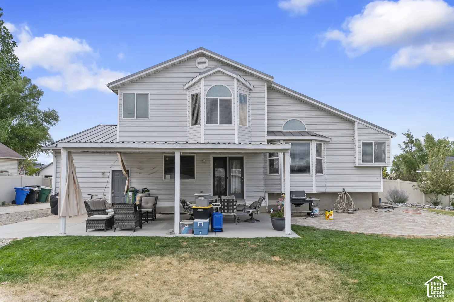Rear exterior featuring light grey siding, a covered patio, and a backyard with a grass lawn and a paved area