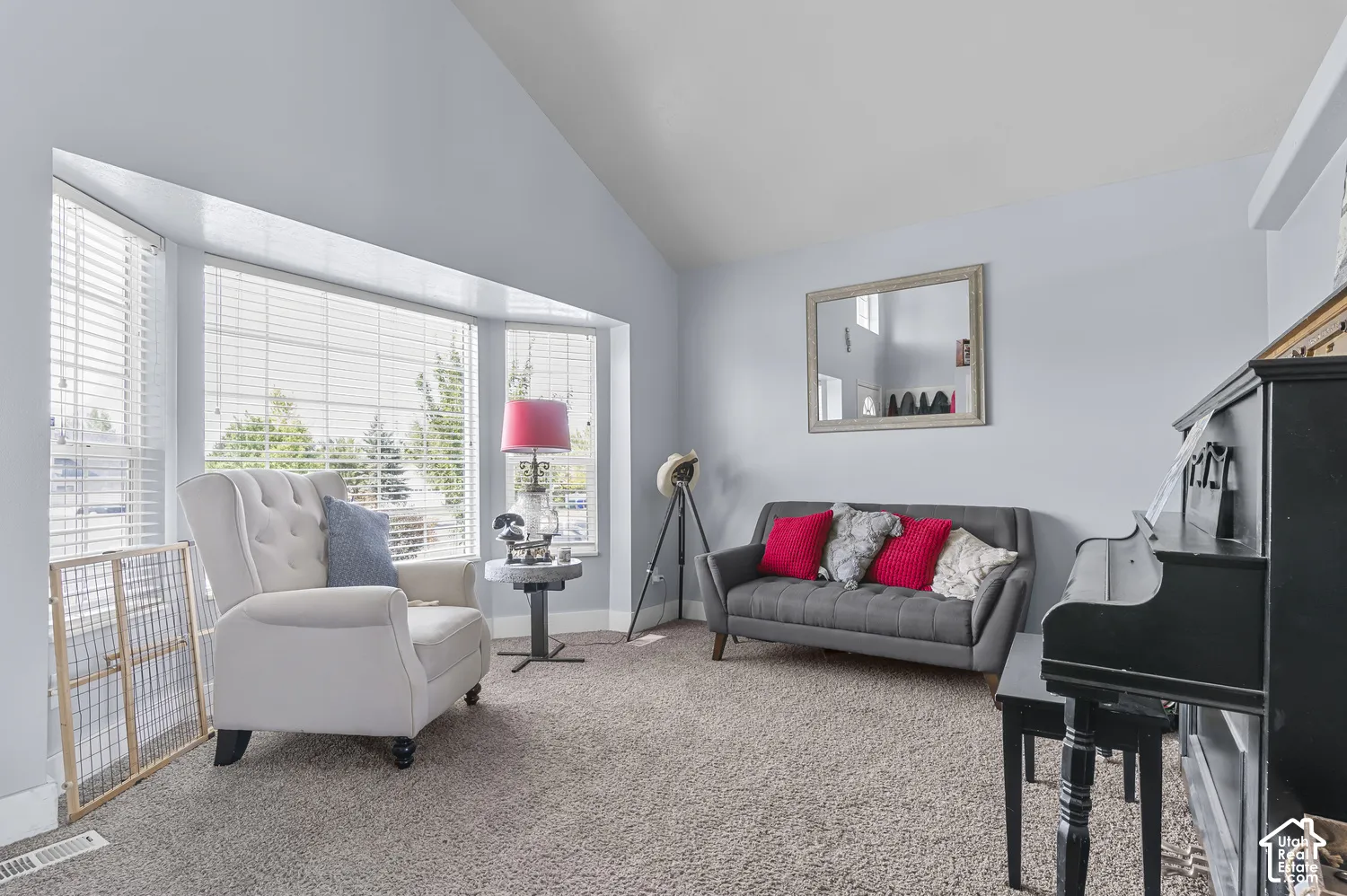 Inviting living area featuring a bay window with blinds, vaulted ceiling, and neutral carpet flooring