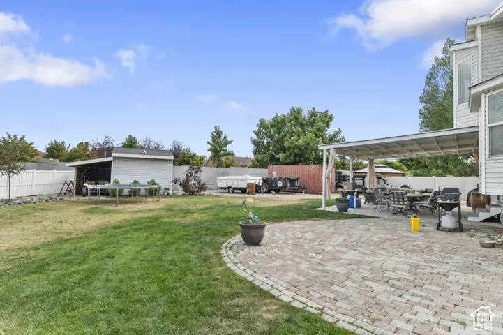 Expansive backyard featuring a spacious paver patio with covered pergola, a manicured lawn area, a functional shed with an open lean-to, and a white picket fence enclosing the perimeter