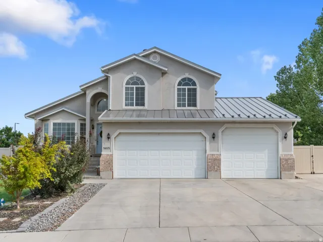 Stucco exterior with a metal roof accent, featuring a dual two-car garage with carriage-style doors