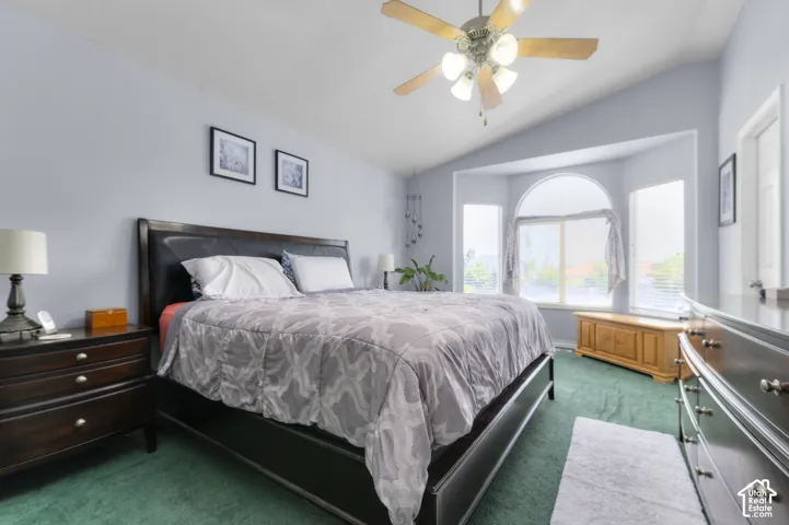 Bedroom featuring a vaulted ceiling with a ceiling fan, a large bay window with an arched transom, and green carpet flooring