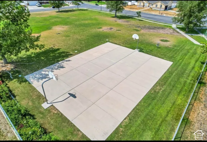 Paved basketball court with two hoops, surrounded by a large grass area and mature trees