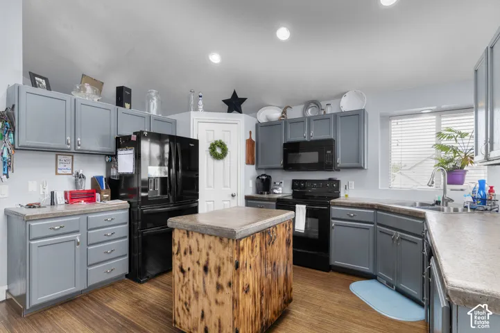 Kitchen featuring gray cabinetry, wood-finish flooring, a wood-panel island, and black appliances