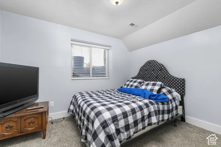 Carpeted bedroom featuring a sloped ceiling and a window with blinds