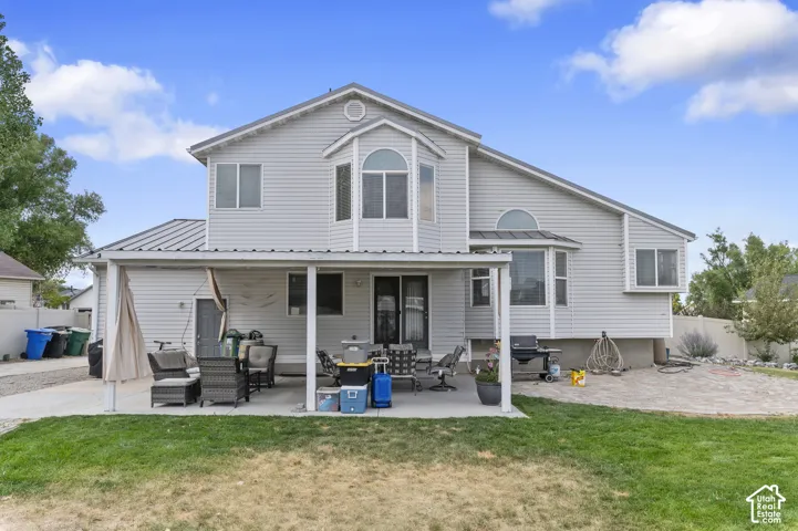 Rear exterior featuring light grey siding, a covered patio, and a backyard with a grass lawn and a paved area