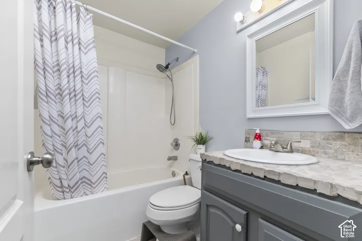 Bathroom featuring a vanity with a drop-in sink, a stacked stone backsplash, and a framed mirror with overhead lighting