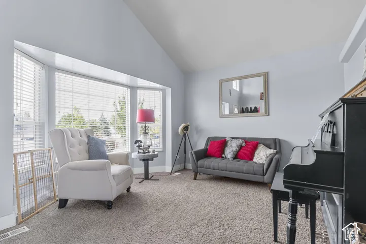Inviting living area featuring a bay window with blinds, vaulted ceiling, and neutral carpet flooring