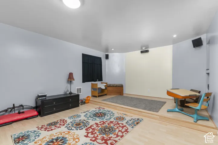 Room featuring a raised platform, wood-finish flooring, recessed lighting, and wall-mounted speakers