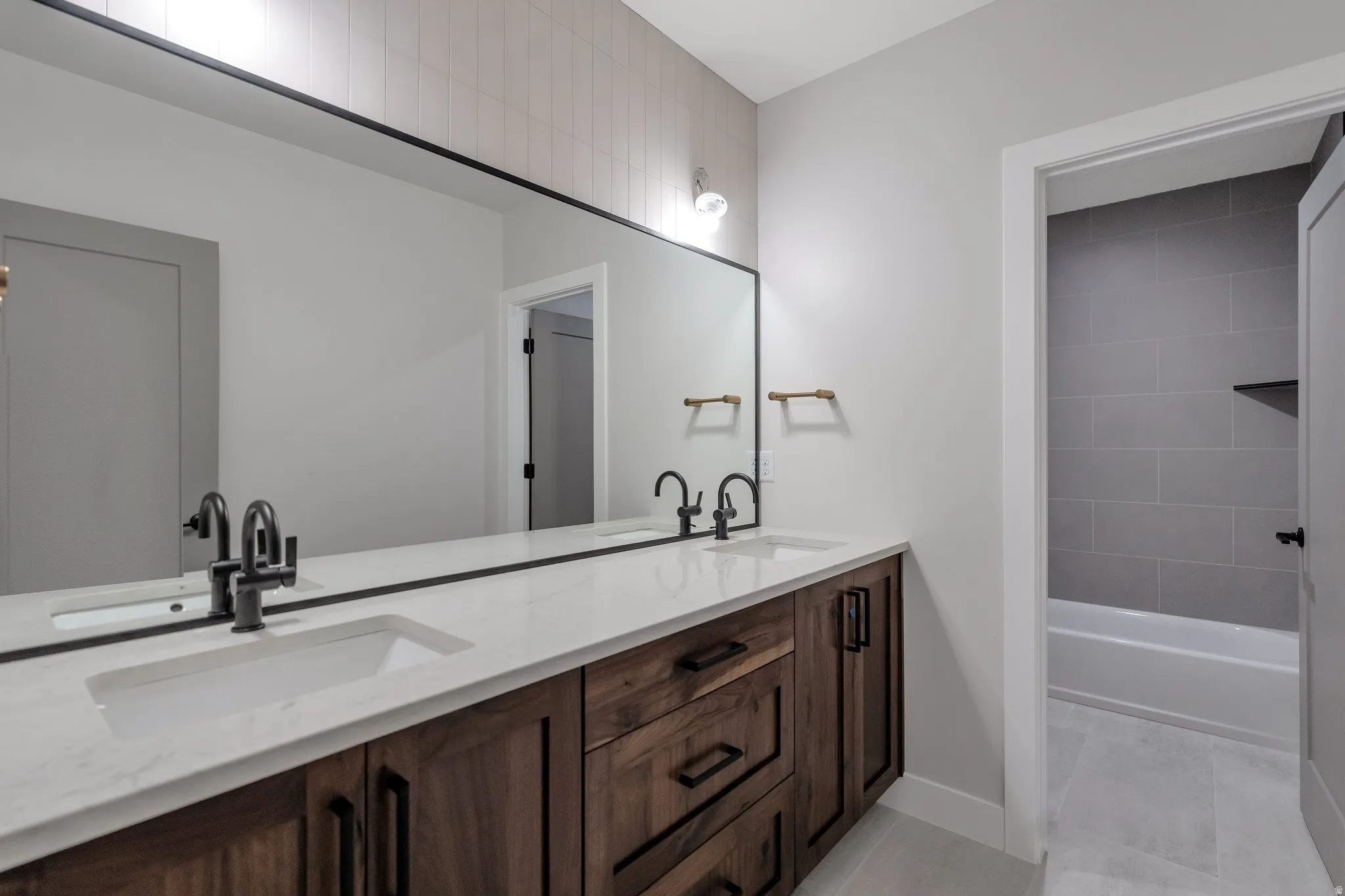 Double vanity featuring wood-finish cabinetry, white countertops, and matte black hardware