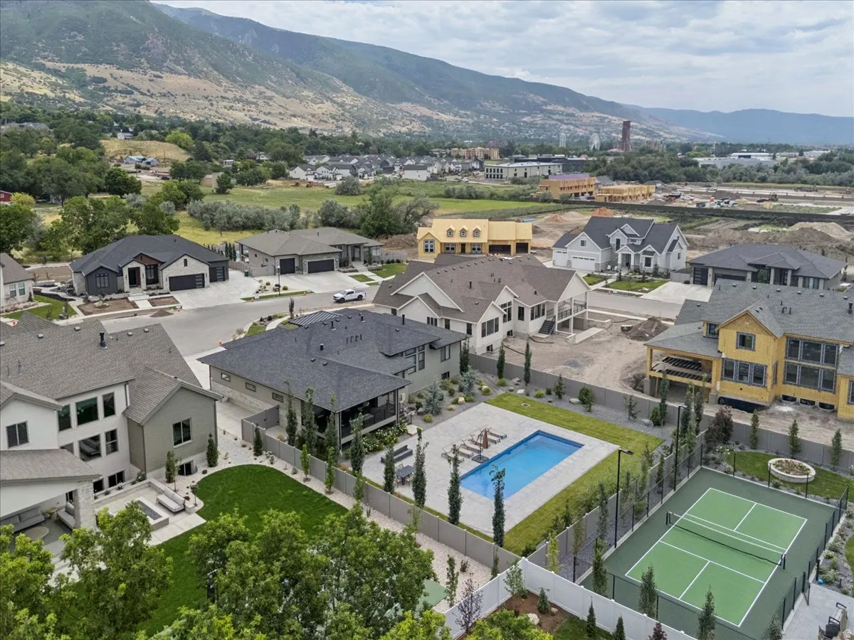 Private tennis court with surrounding fencing, adjacent swimming pool, manicured lawn, and mature landscaping
