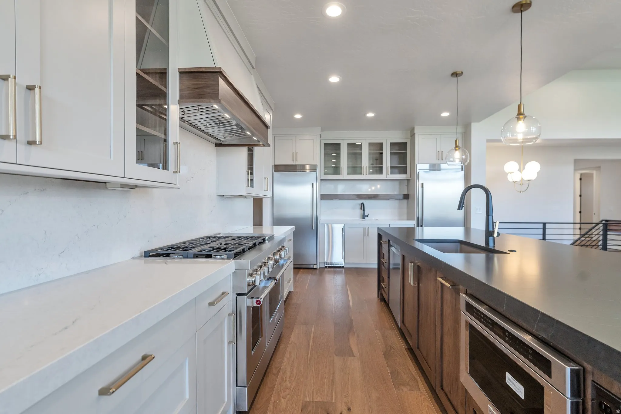 Gourmet kitchen featuring a large island with an undermount sink, stainless steel appliances, wood-finish flooring, white cabinetry, and recessed lighting