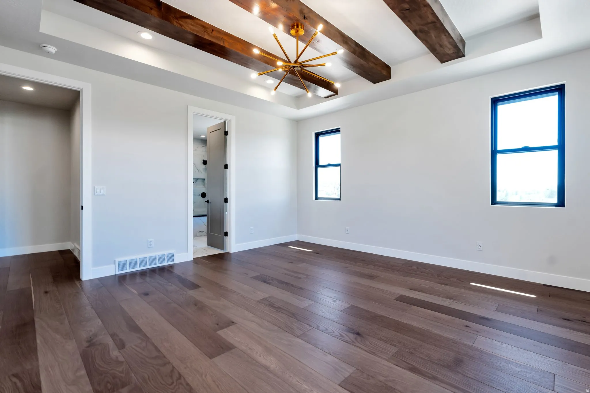 Spacious room featuring wood-finish flooring, a coffered ceiling with exposed wood beams, and a modern chandelier