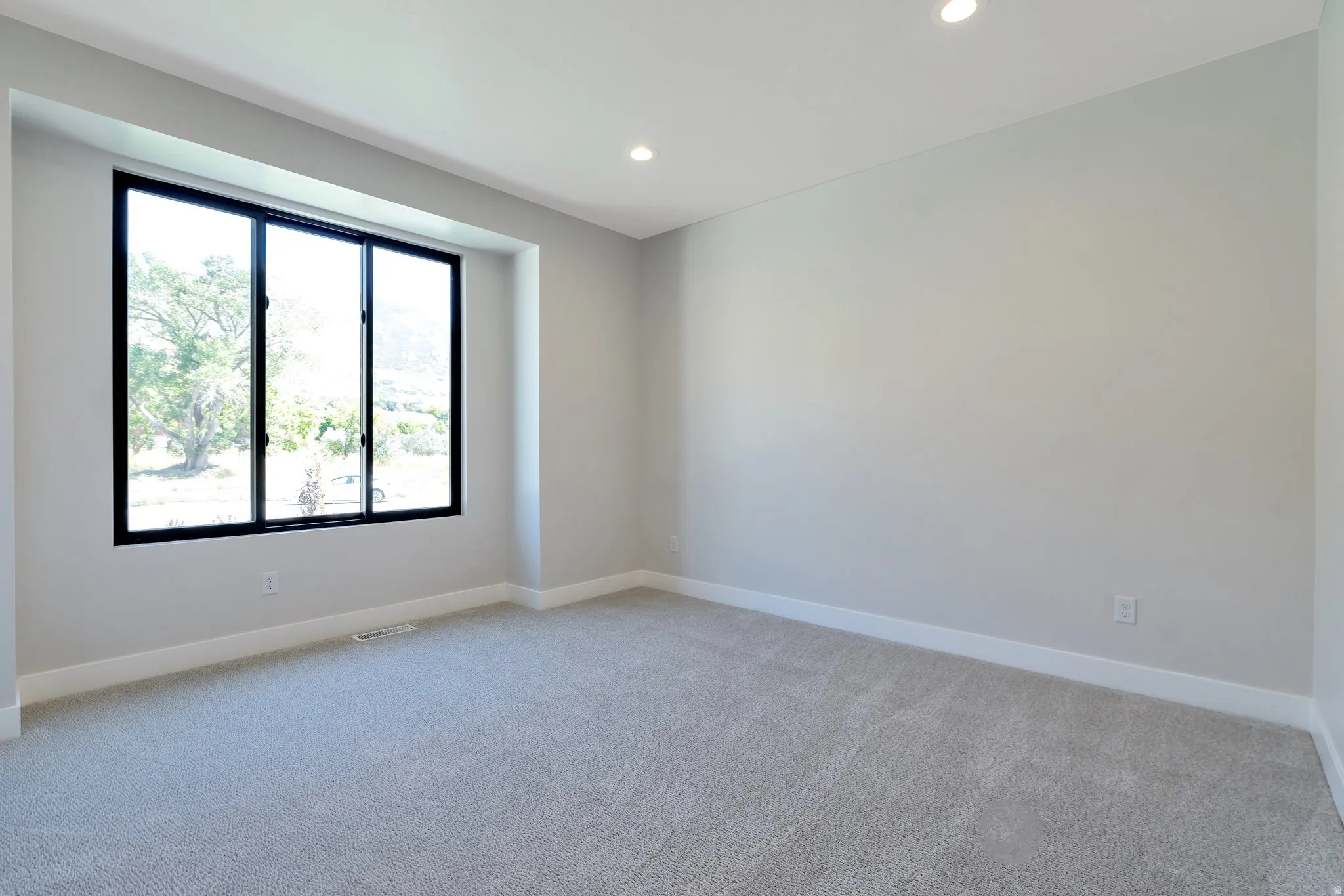 Recessed window with black framing, light gray wall paint, light gray carpet, white baseboards, and recessed ceiling lighting