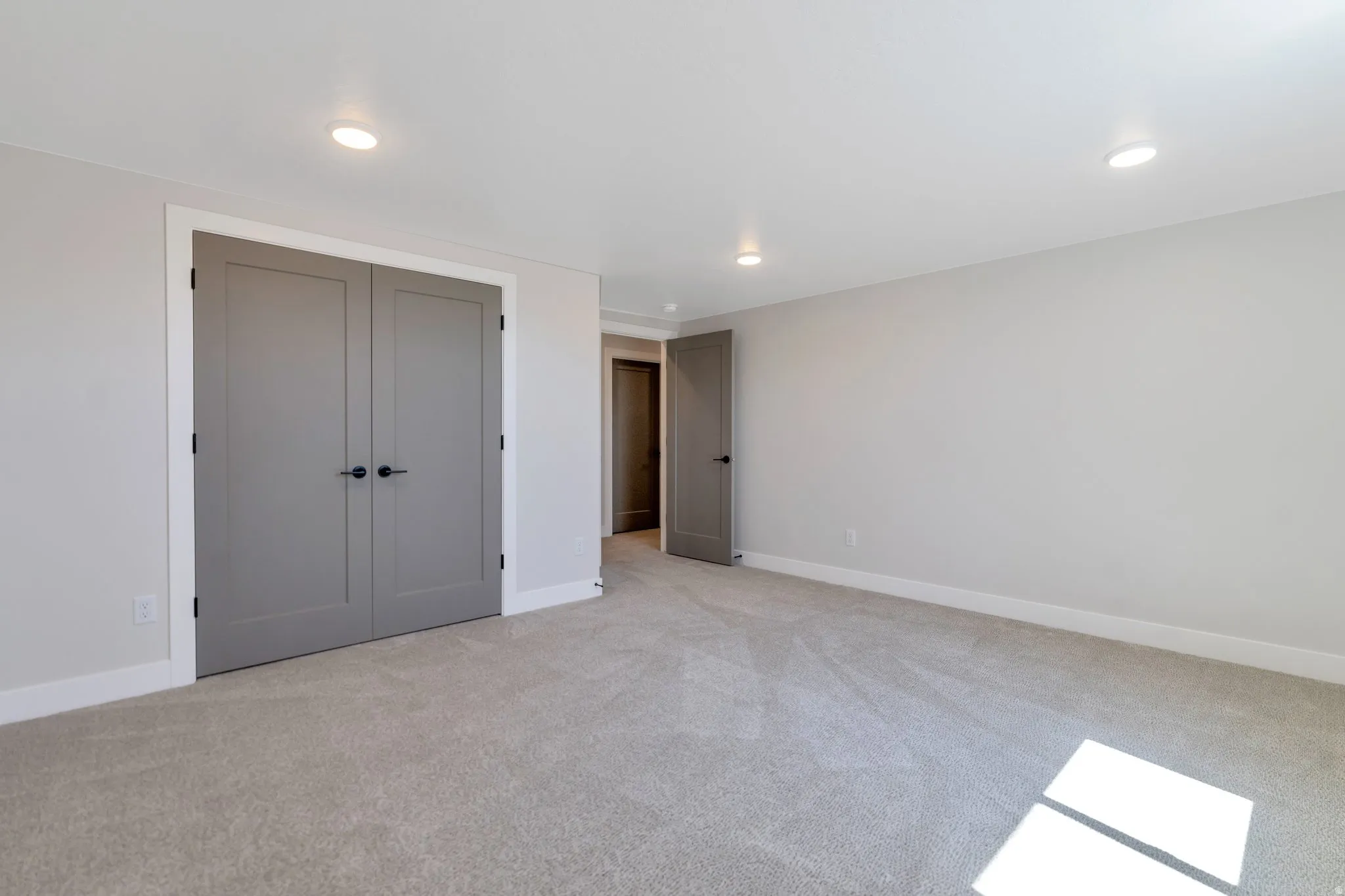 Spacious room featuring neutral carpeting, recessed ceiling lighting, and a pair of modern paneled doors with black hardware