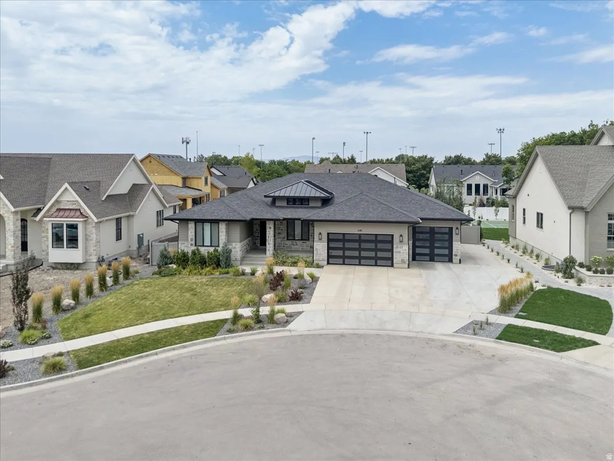 Contemporary single-story residence featuring a dark gray roof, stucco and stone exterior, two modern garage doors with frosted glass panels, an arched entry portico, and a concrete driveway