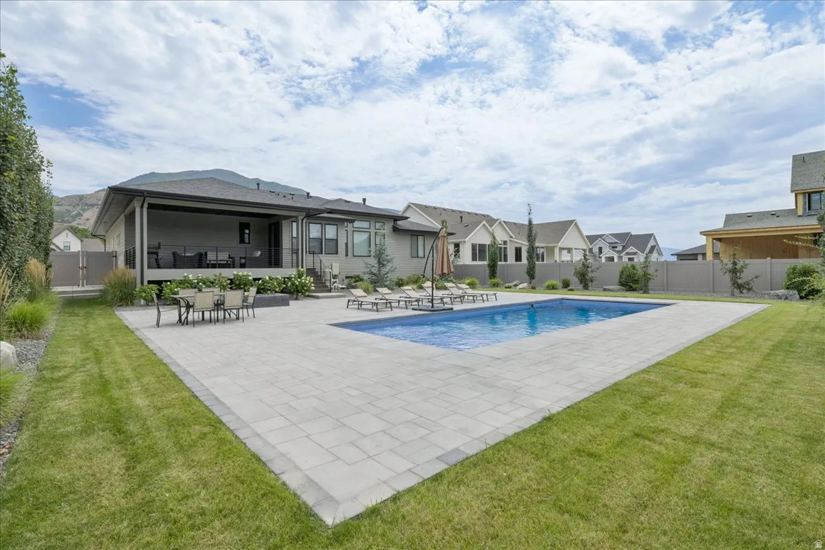 Expansive backyard featuring a rectangular swimming pool, large paver patio, and a covered patio area with a dark railing