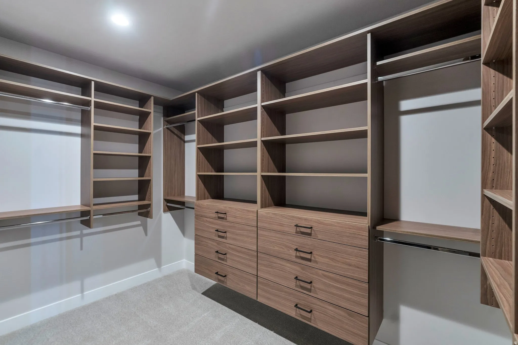 Custom closet system featuring wood-finish shelving, multiple hanging rods, and integrated drawer units with matte black hardware