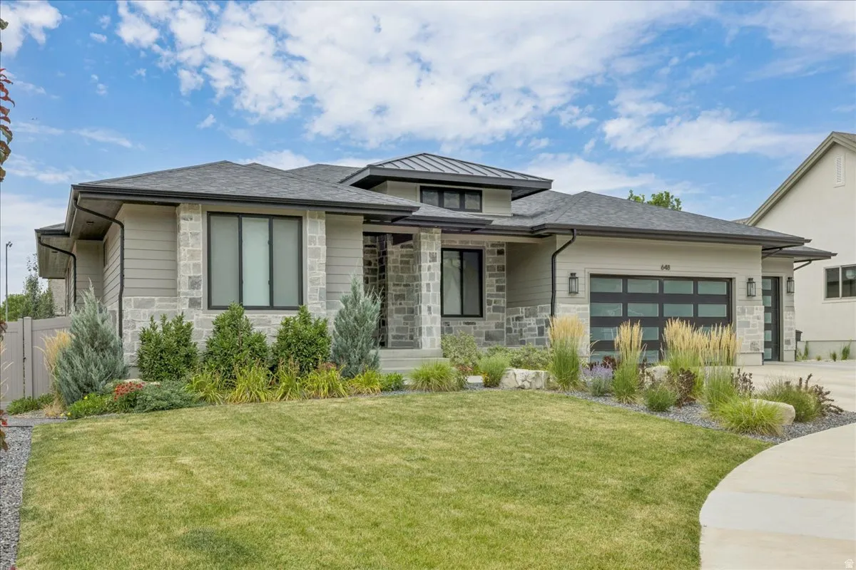 Contemporary exterior featuring stone accents, horizontal siding, dark-framed windows, a modern garage door, and a manicured lawn with varied landscaping