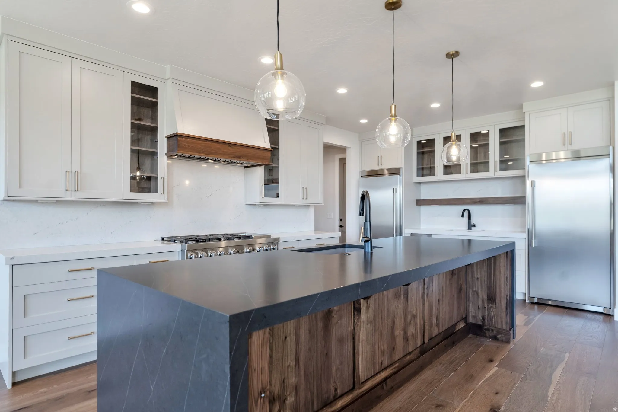 Expansive kitchen featuring a large island with a dark countertop and wood-finish cabinetry, stainless steel appliances, white perimeter cabinetry, a white tile backsplash, and recessed lighting