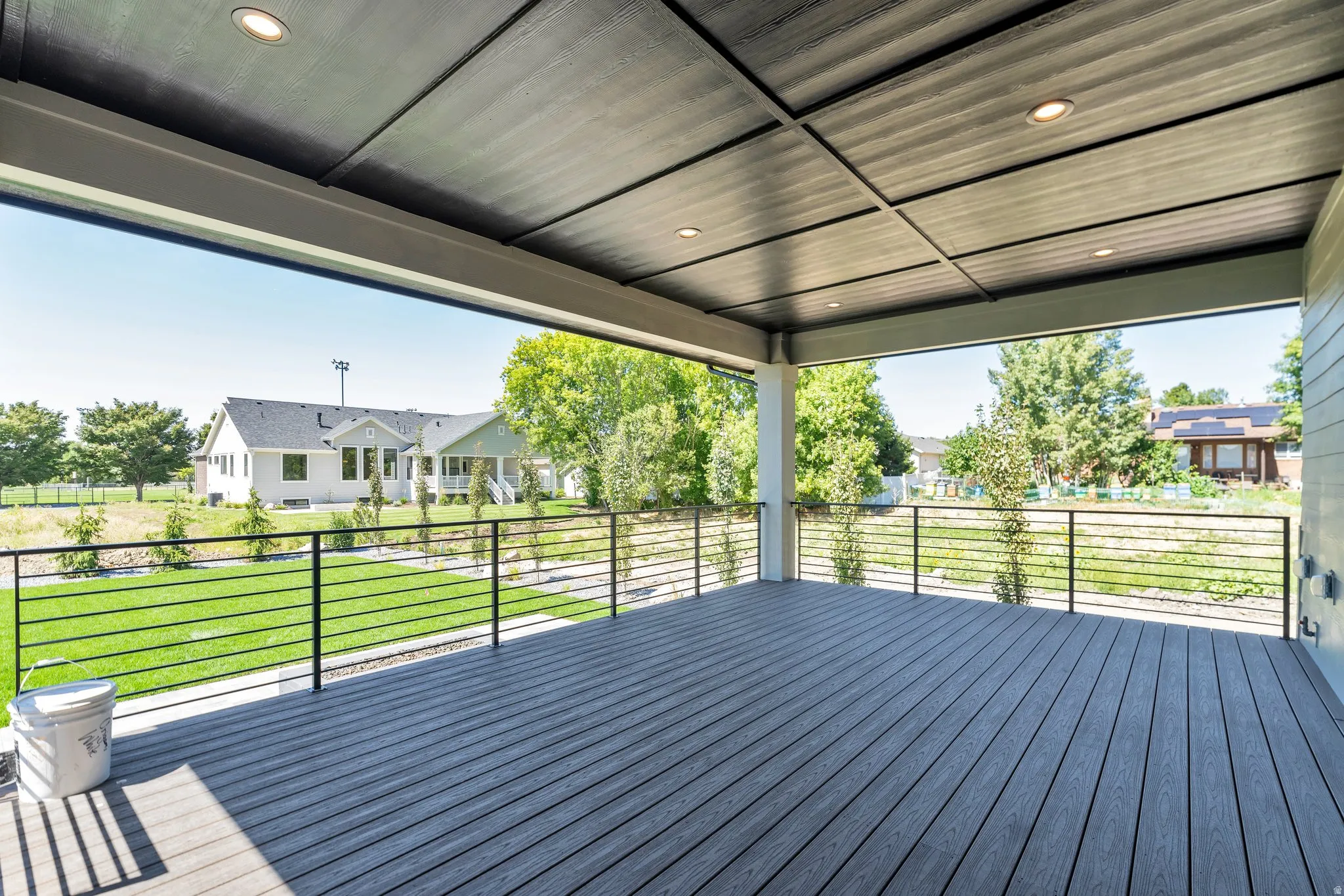 Spacious covered patio featuring composite decking, recessed lighting, and modern black horizontal bar railings