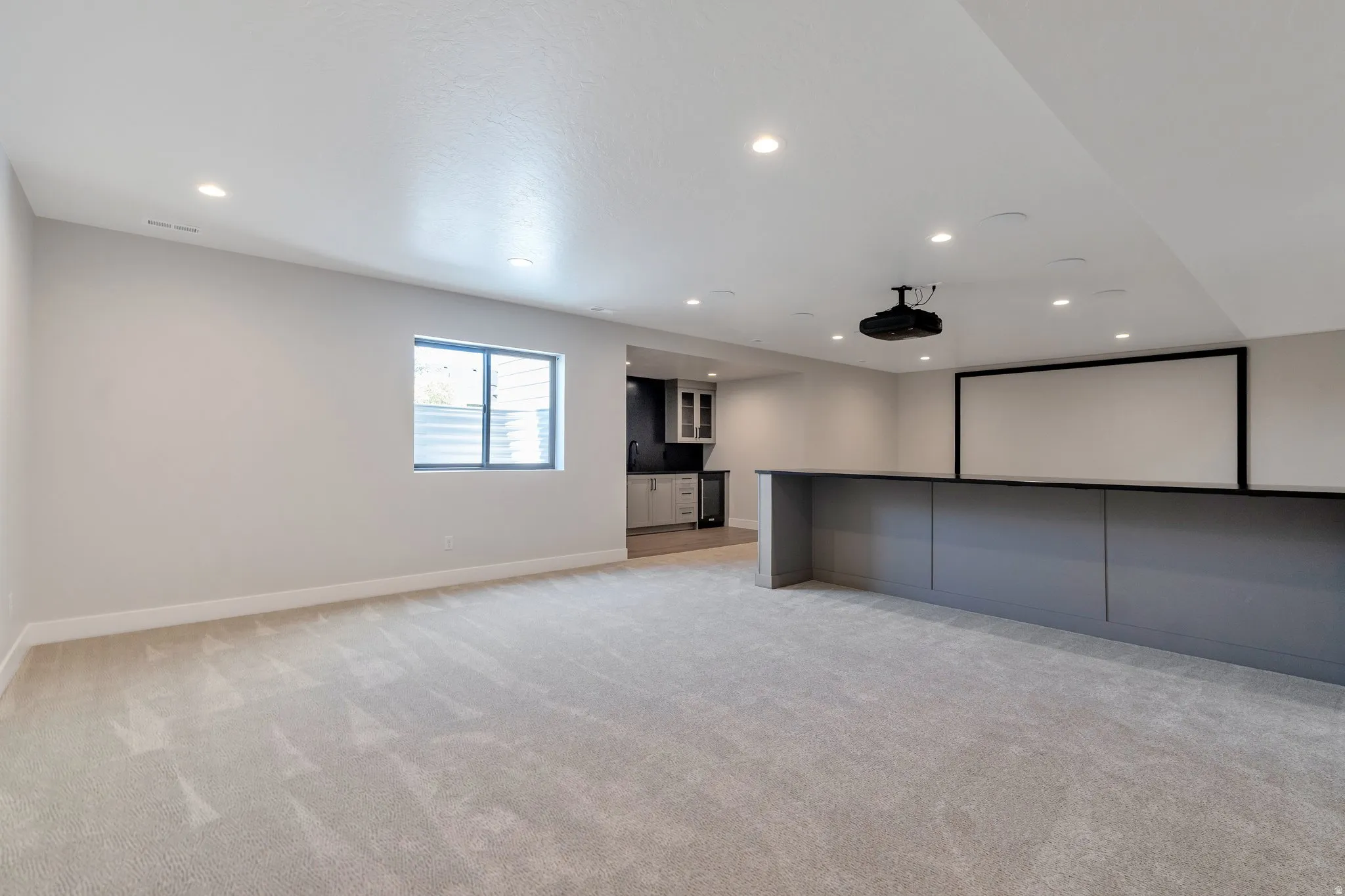 Spacious entertainment area featuring a built-in media screen, overhead projector, recessed lighting, and a wet bar with shaker cabinetry