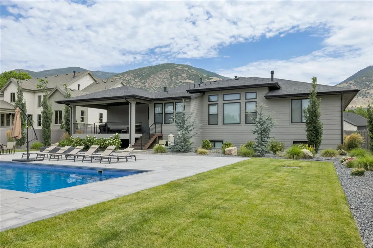 Expansive backyard featuring a rectangular swimming pool, concrete paver patio, and a covered outdoor living area with stairs