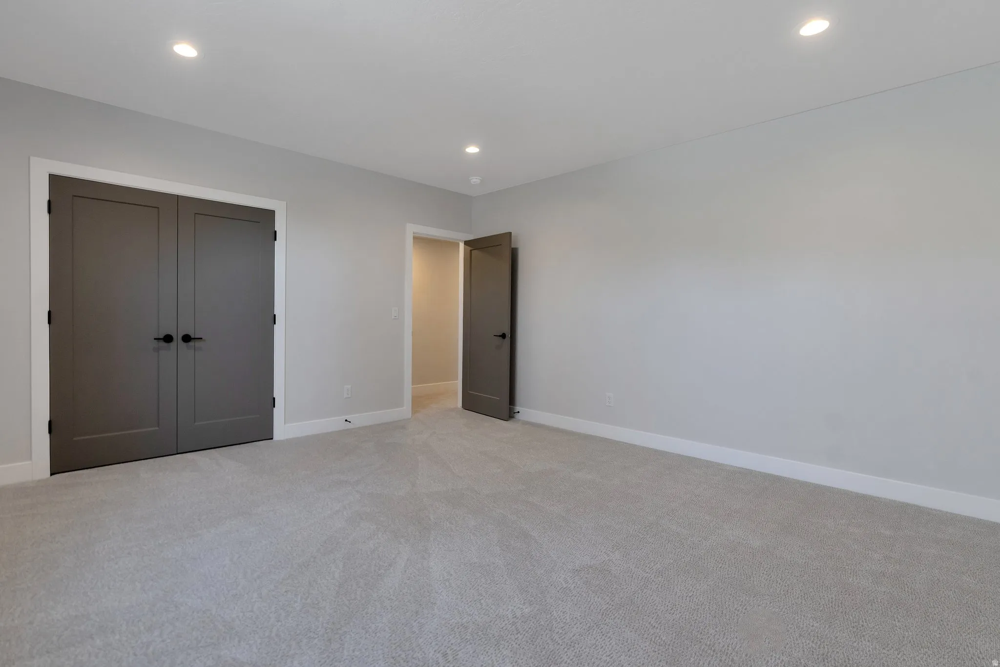 Neutral-toned room featuring a light gray carpet, recessed lighting, and a double-door closet with dark gray doors and matte black hardware