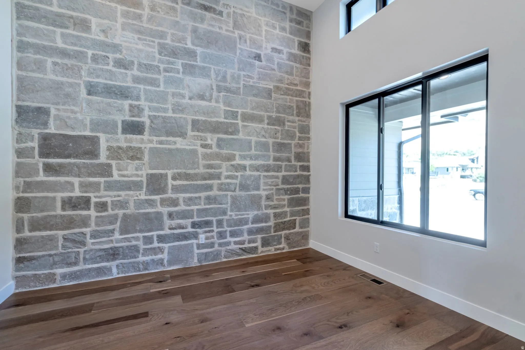 Stone accent wall, wood-finish flooring, tall ceilings, and large windows with black frames