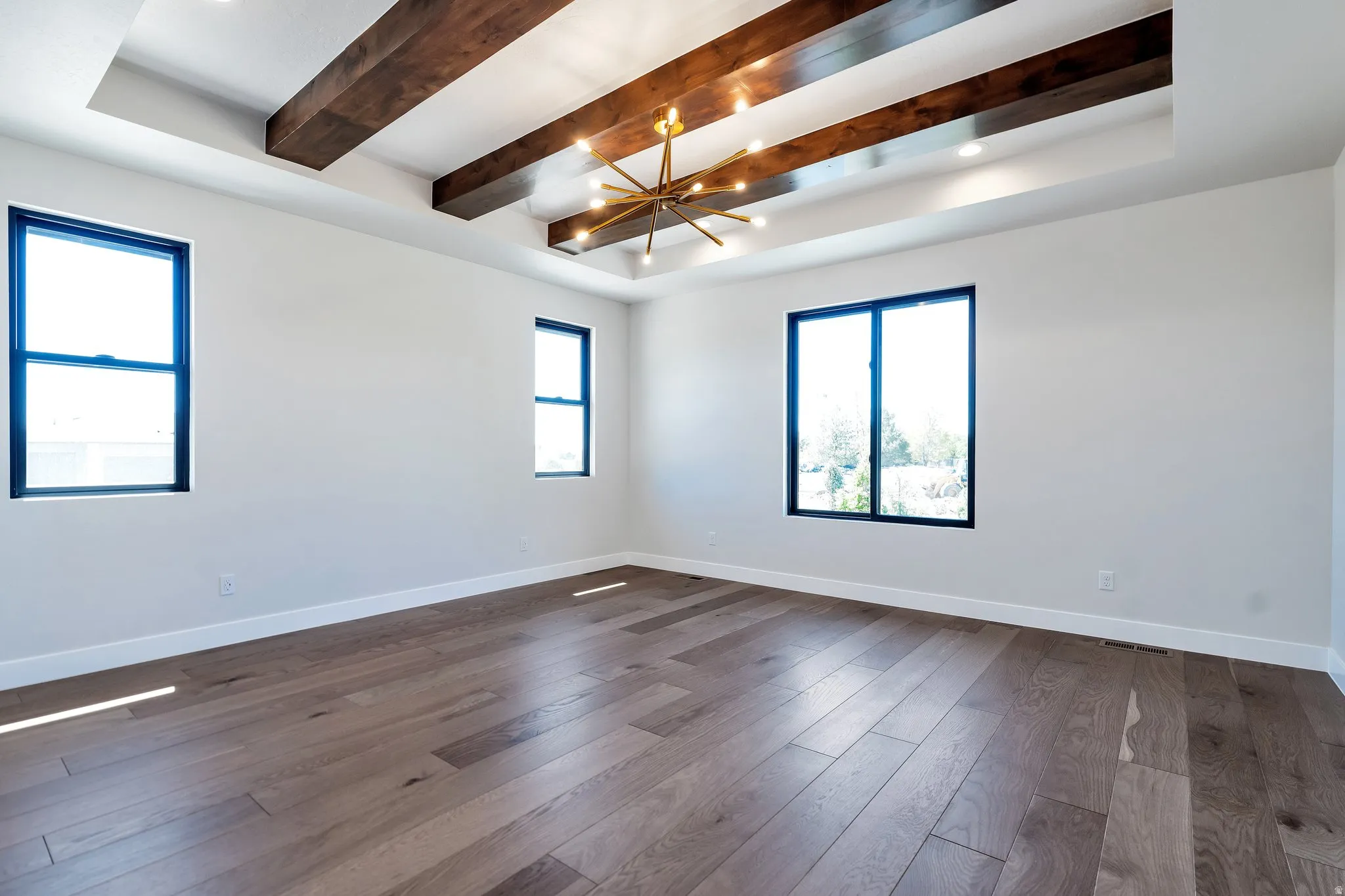Spacious room featuring wood-finish flooring, recessed lighting, a tray ceiling with exposed wood beams, and a contemporary chandelier