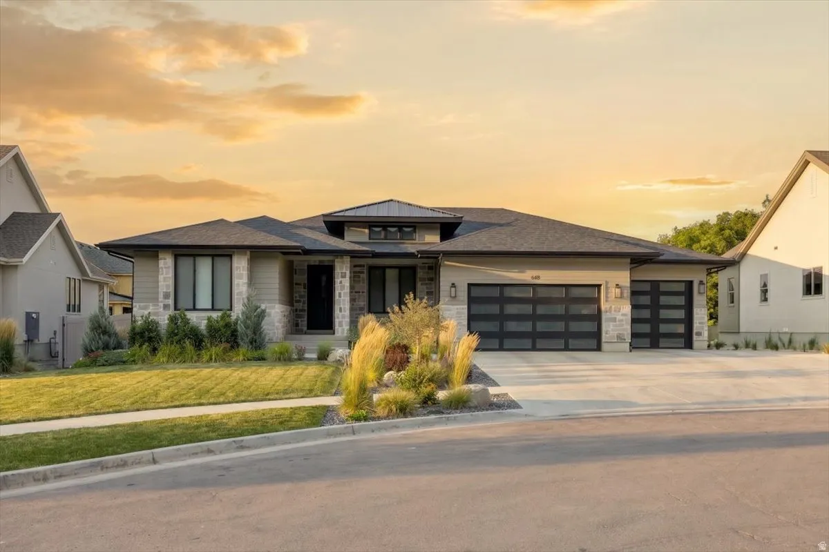 Modern residence featuring a stone and stucco exterior, prominent dark-framed windows, and a multi-car garage with contemporary glass panel doors